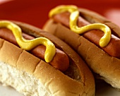 Two hot dogs side by side with mustard 