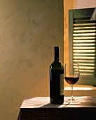 Red wine in bottle and glass on table in front of a window