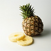 A pineapple and two slices of pineapple