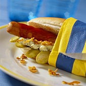 Hot dog with pickled gherkin and ketchup in coloured napkin
