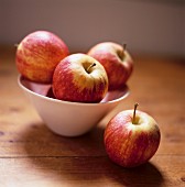 Red apples in a bowl and one beside it on a wooden table