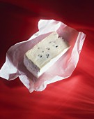 Blue-veined cheese in paper on a red background