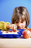 Kleines Mädchen legt Apfelstücke in Teig