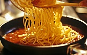 Mixing spaghetti with tomato sauce in frying pan