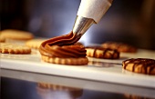 Piping chocolate cream on biscuits