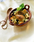 Chicken leg with vegetables in ceramic pot beside wooden spoon