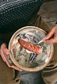 Mann hält Topf mit in Fett konservierten Würsten (Savoyen)