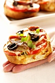 Hand holding mini-pizza with tomatoes, olives and anchovies