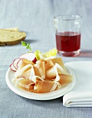 Schinkenspeck and radishes on plate; glass of red wine