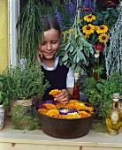 Girl at window with flowers, herbs and herb oils