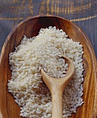 Arborio rice in wooden bowl with kitchen spoon