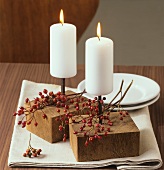 Table decoration: white candles and branch of rose hips