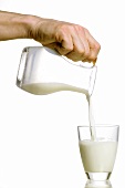 Hand giesst Milch aus Karaffe in Glas
