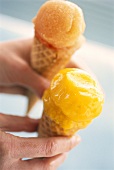 Hands holding two cones of fruit ice cream