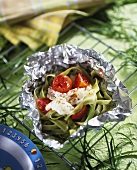 Green ribbon pasta with cod and tomatoes in aluminium foil