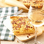 Onion quiche with bacon on chopping board; glass of white wine