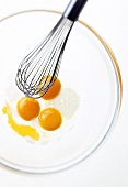 Three eggs broken into glass bowl, with whisk