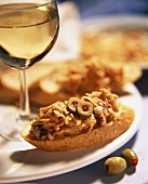 Baguette snacks with carrot and anchovy topping and olives