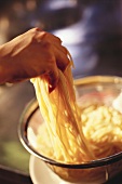 Hand hebt gekochte Spaghetti aus einem Sieb