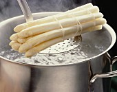 A bundle of asparagus on a skimmer over boiling water