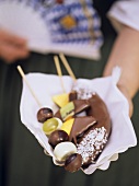 Woman in national dress with chocolate-coated fruit kebab
