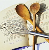 Whisk and wooden spoons on recipe book