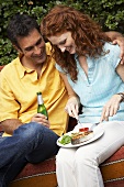Woman eating barbecued salmon cutlet, man drinking beer