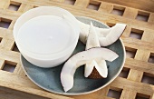 Bowl of coconut milk, beside three pieces of coconut