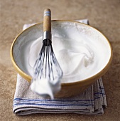 Beaten egg white in a bowl with a whisk