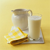 Glass of fresh milk in front of pottery jug