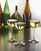 Drei Gläser Weißwein vor Weinflaschen