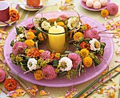Wreath of zinnias around wind light with yellow candle