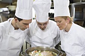 Three chefs examining the contents of a pan