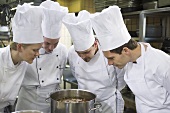 Four chefs examining the contents of a pan