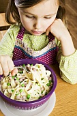 Girl eating ribbon pasta with ham & peas, without enthusiasm
