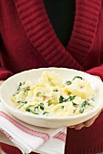 Woman holding plate of tortellini with spinach & cream sauce