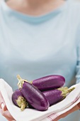 Woman holding fresh aubergines on tea towel