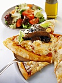 Slice of pizza with mushrooms on server, salad in background