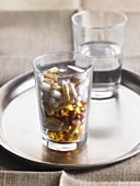 Glass of assorted capsules & tablets in front of glass of water