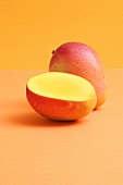 Whole mango and half a mango on coloured background
