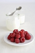 Fresh raspberries on plate, jars of yoghurt in background