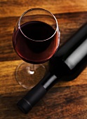 Glass of red wine beside red wine bottle on wooden surface