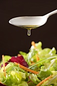Olivenöl tropft vom Löffel auf gemischten Blattsalat