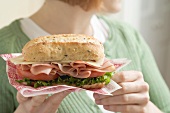 Frau hält Schinken-Käse-Sandwich auf Papierserviette