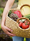 Woman holding bag of freshly picked vegetables in garden