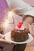 Woman holding small chocolate cake with sparkler