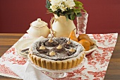 Pear and chocolate tart on cake stand, jug of roses