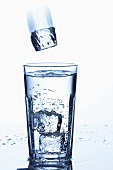 Eiswürfel fällt in ein Glas Mineralwasser
