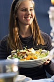 A smilling young woman holding a plate of bread salad with fennel and mandarins