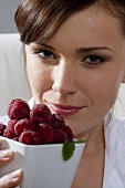 Young woman holding bowl of fresh raspberries